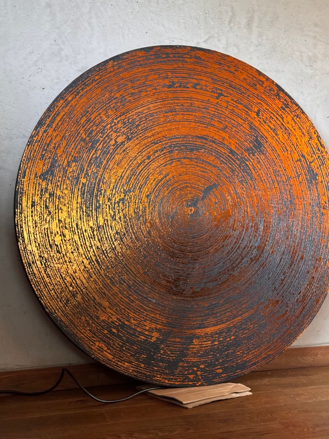 Bronze circular GLO Panel with concentric trowel marks on a pale wall