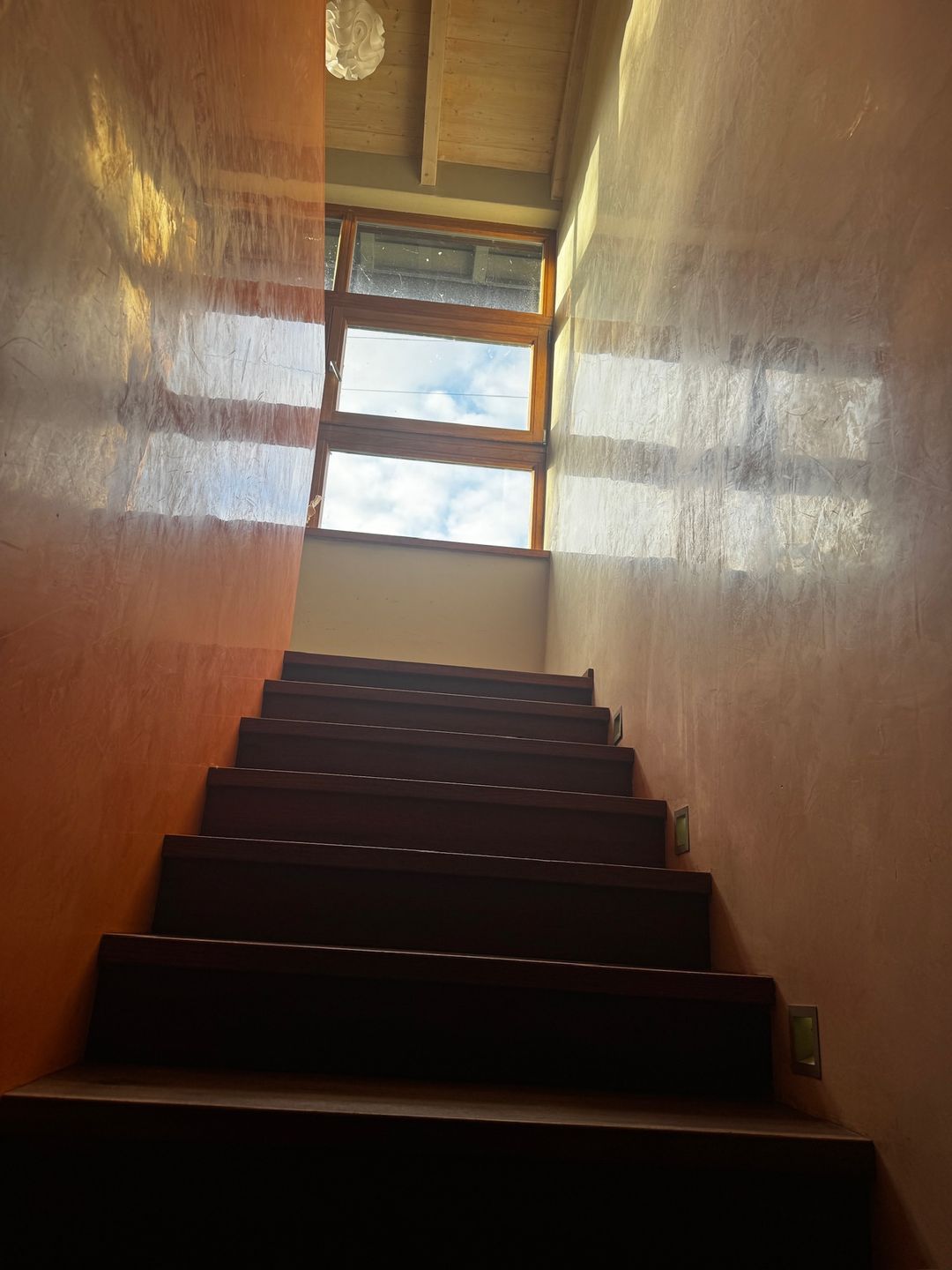A stairwell finished in warm Spatula Stucchi catching light from the window